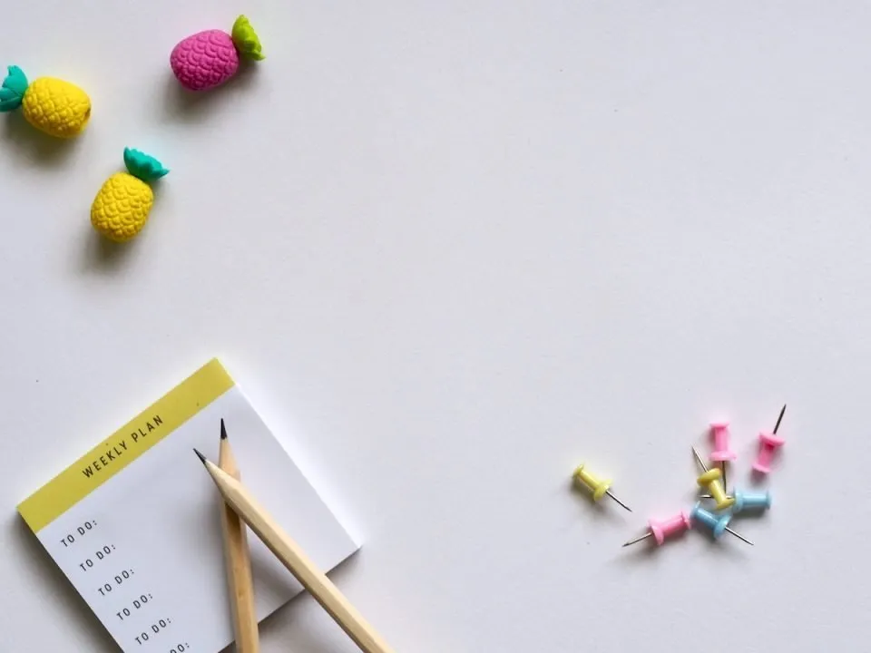 A to-do list, brown pencils, and pastel push-pins on a white background. (Pexels/Jess Bailey)