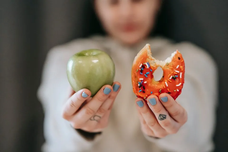 Someone holding an apple in one hand and a donut in the other.