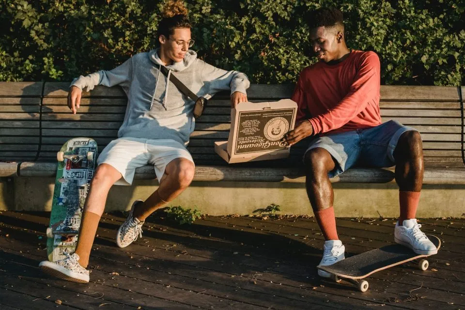 Two people on a park bench sharing a pizza.