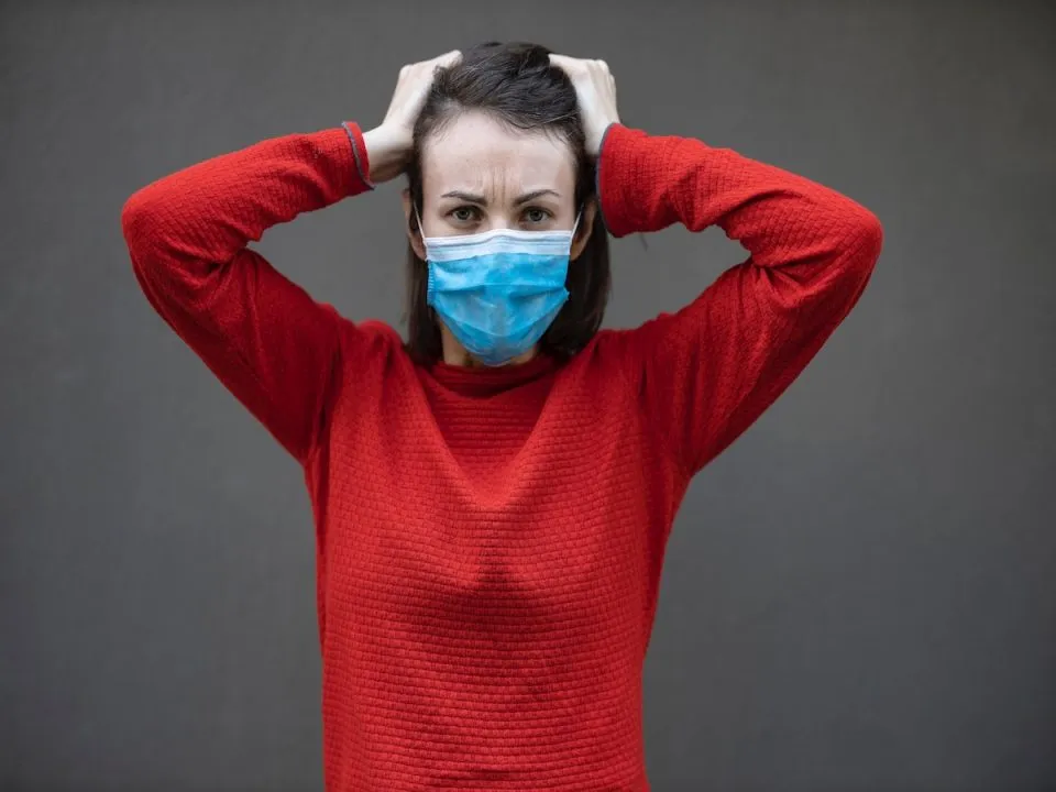 A woman in a face mask and a sweater looking frustrated. (Pexels/Engin Akyurt)