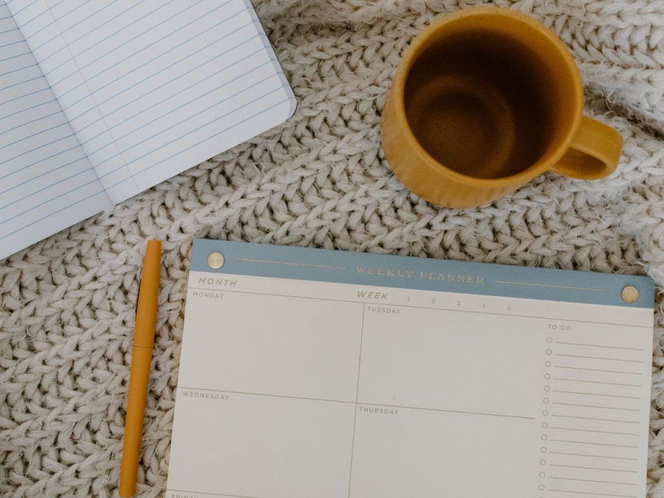 A planner, notebook, pencil, and mug sit on a table. (Canva)