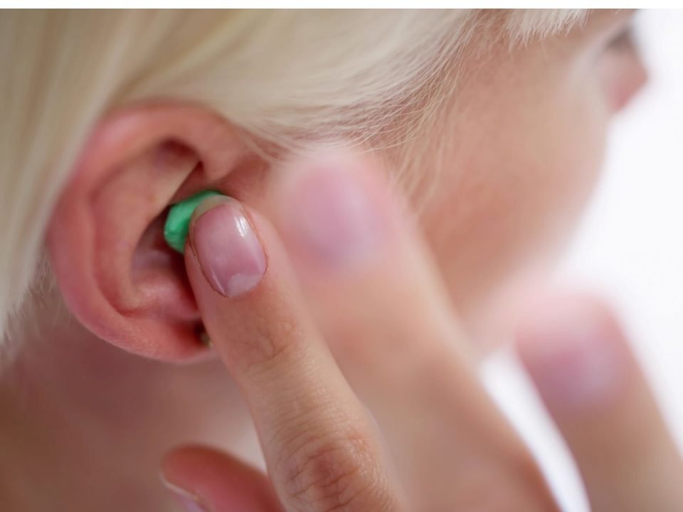 Someone putting an earplug in their ear. (Canva)