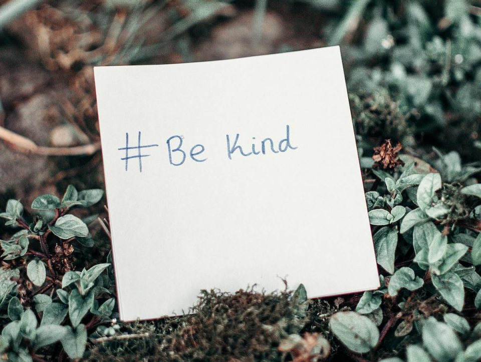 A post-it note on a lush, plant-covered floor that says "be kind." (Lisa Fotios/Pexels)