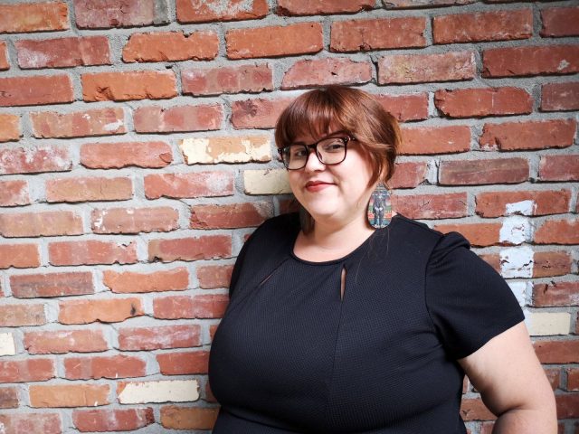 Portrait of Joni Oldhoff against a brick wall.