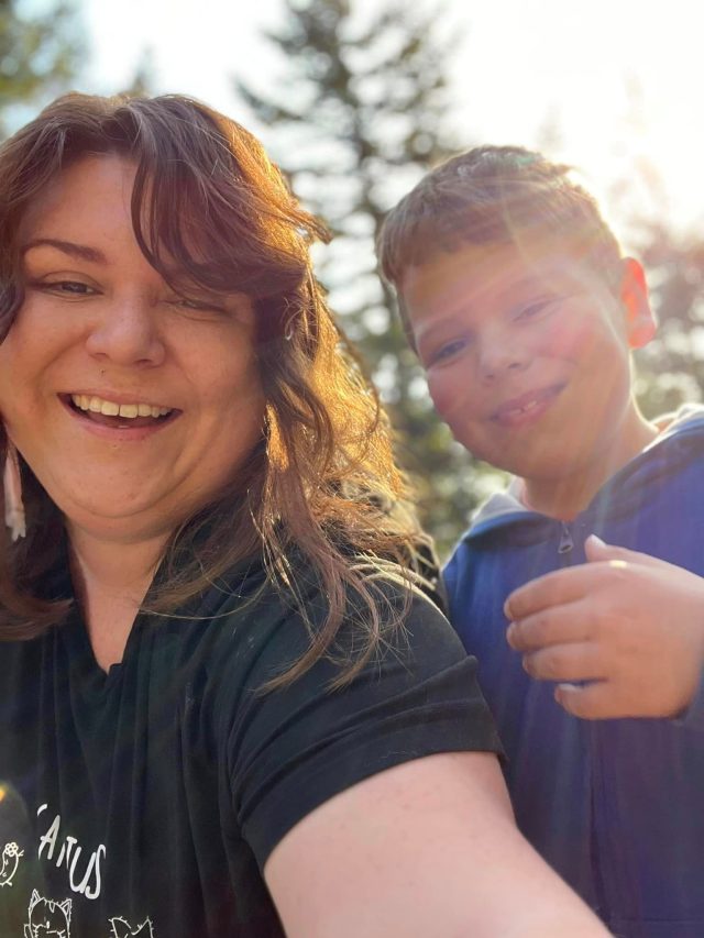 Joni and her son smiling in sunlight with trees in the background.