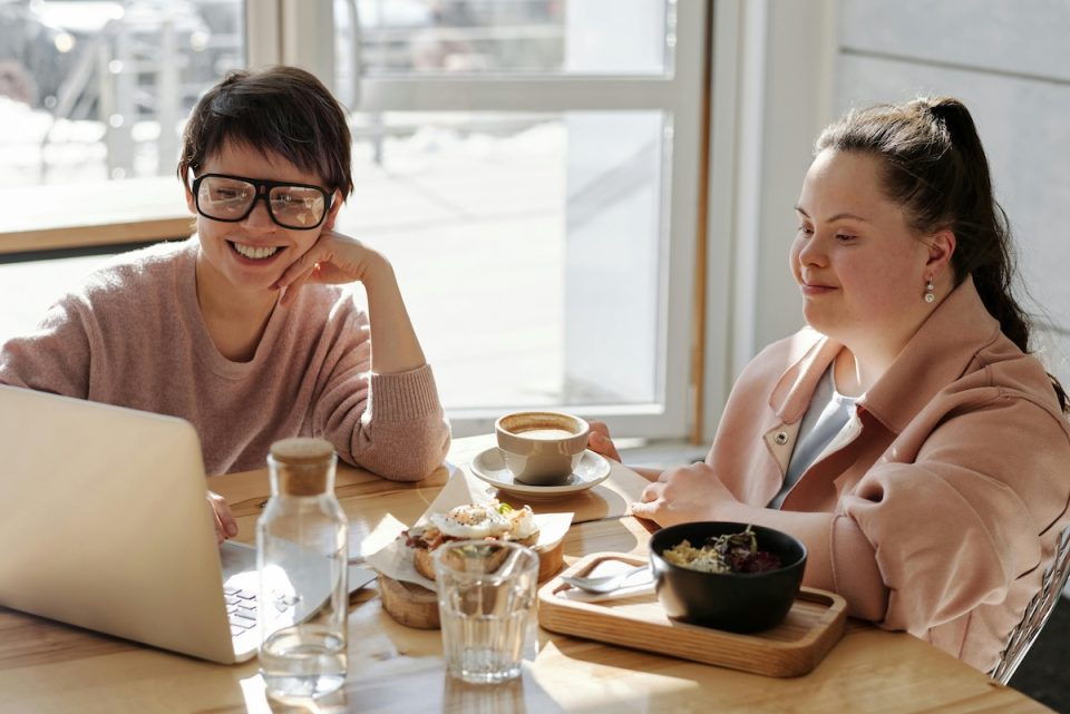 Two people talking over coffee and laptops. (Cliff Booth/Pexels)
