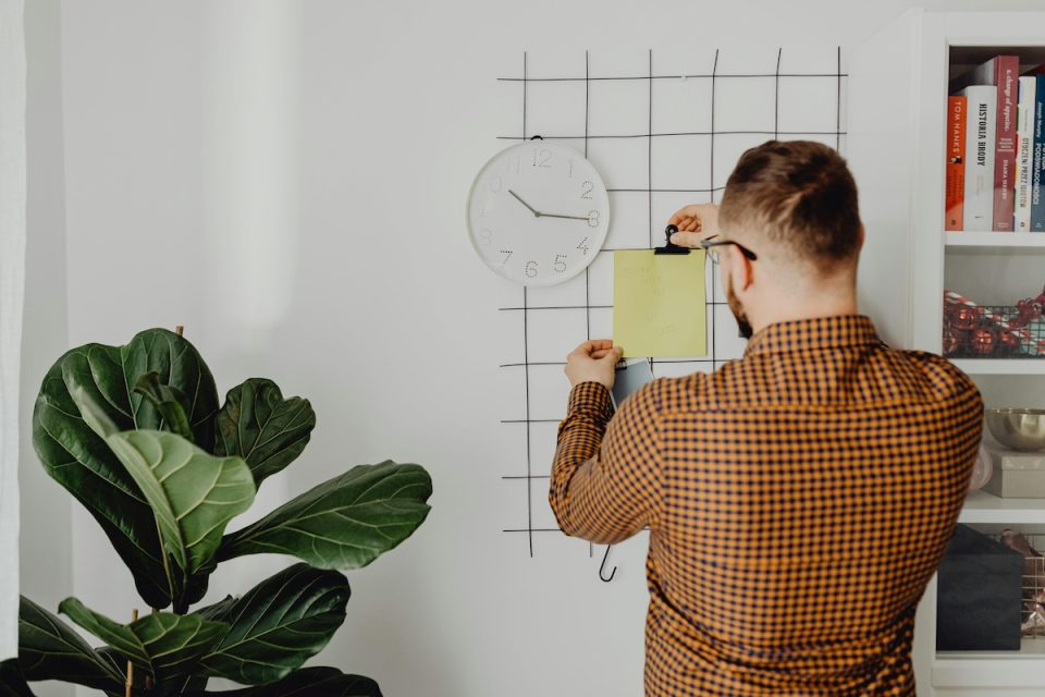 Someone putting a note up on a schedule board at home. (Karolina Grabowska/Pexels)