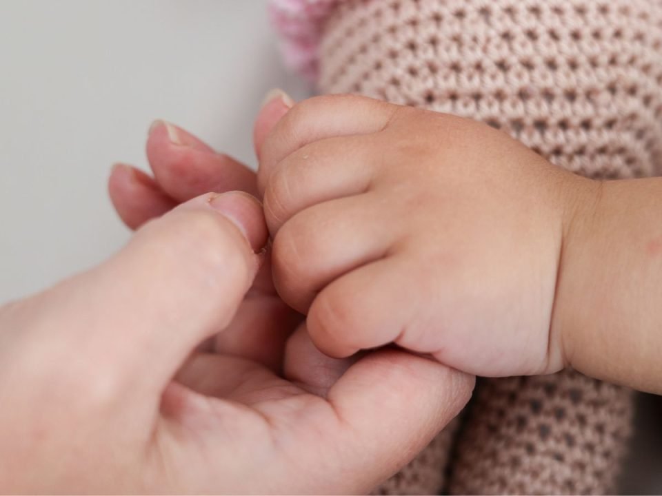 A close-up shot of a baby and parent holding hands. (Canva)