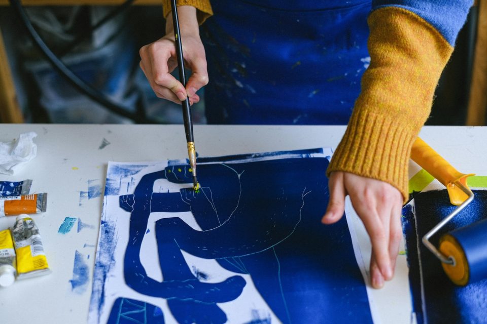 An artist's hands painting on a canvas. The paint is indigo blue. (Anna Shvets/Pexels)