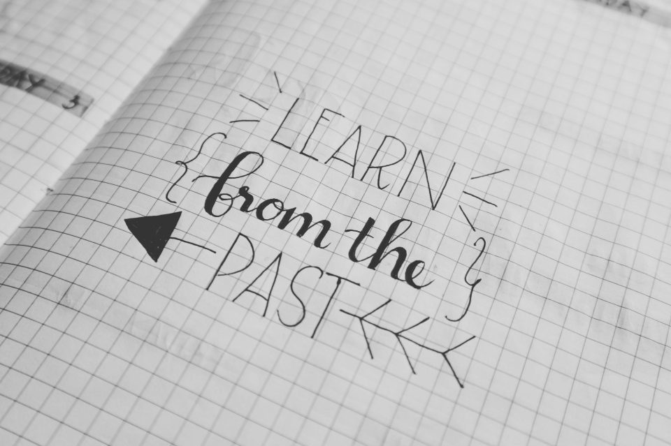 Ink typography on gridded paper reads, "Learn from the past." (Bich Tran/Pexels)