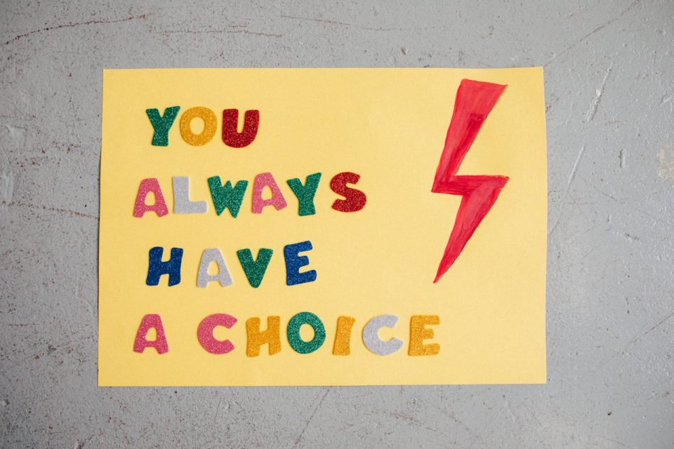 A handmade, yellow poster reading "You always have a choice" in colorful block letters. A red lightning bolt is beside the text. (Pexels/Viktoria Slowikowska)