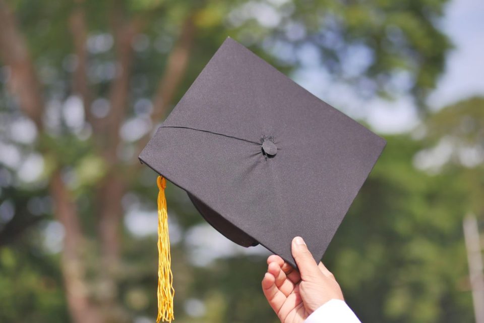 A hand holding a graduation cap to the sky outdoors. (Towfiqu barbhuiya/Pexels)